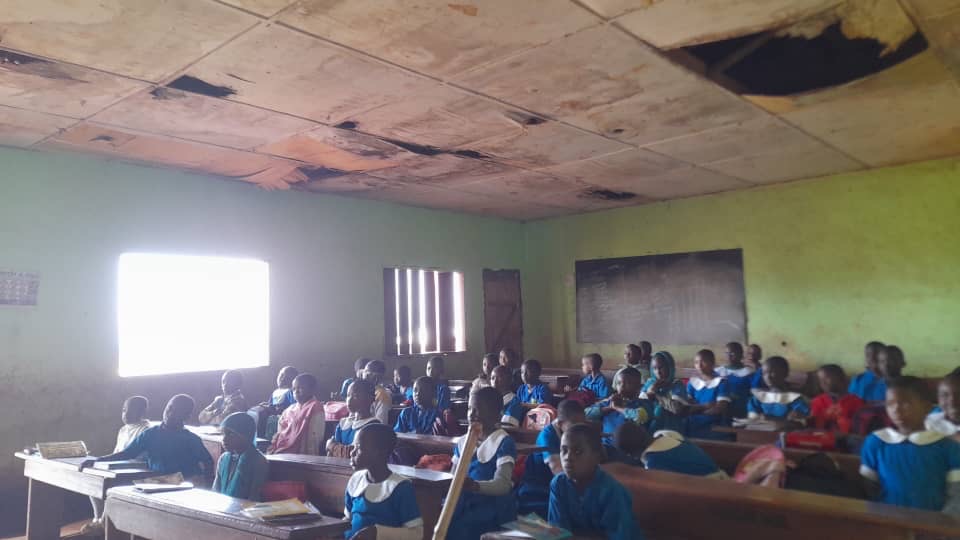 Pupils learning in a classroom beneath a deteriorated ceiling at GBPS Bafoussam Group 2B before intervention